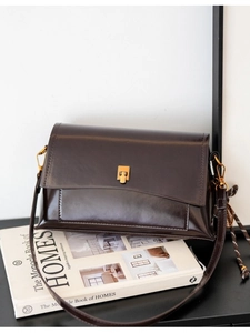 Sac carré vintage en cuir huilé marron foncé avec boucle dorée sur des livres d'art