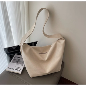 Minimalist beige hobo bag with wide strap displayed next to a laptop and design book