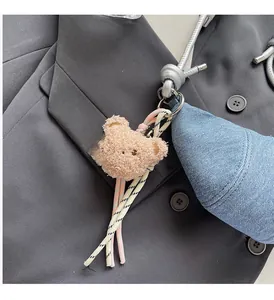 Detail eines flauschigen Bären-Plüsch-Anhängers mit buntem geflochtenem Band an Tasche