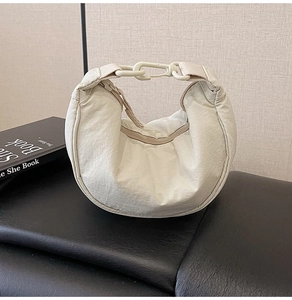 Macro detail of creamy white nylon crescent bag with textured surface and sleek buckle