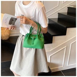 Detail of emerald green woven bucket bag held by a model in a minimalist setting