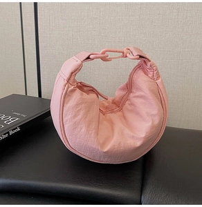 Close-up of a pink nylon hobo bag with unique chunky chain handle on a leather surface