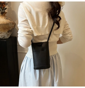 Detail van een kleine zwarte crossbodytas met litchi-textuur gedragen door een model