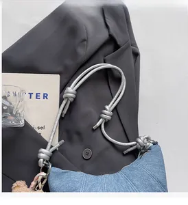 Detail einer blauen Denim-Halbmondtasche mit geknotetem silbernem Riemen und Bär-Anhänger