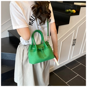 Detail of green woven bucket bag with smooth leather finish and metallic buckle on the strap