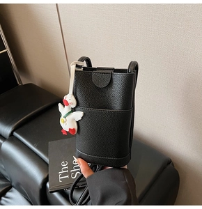Detail of black litchi grain leather mini crossbody bag with a cute duck charm