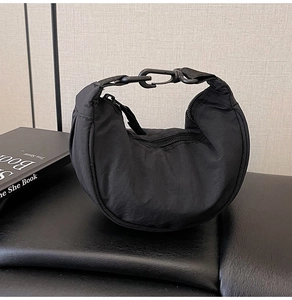 Detail of black crescent crossbody bag showing nylon texture and metal carabiner buckle