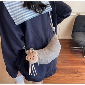 Detail der grauen halbmondförmigen Tasche mit Aufdruck und süßem Bärenanhänger-Dekor