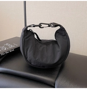 Detail of black nylon crescent bag with metal buckle on leather base next to a book
