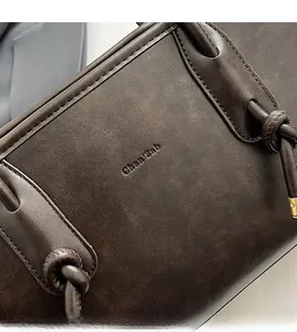 Dettaglio della texture in pelle granulata marrone scuro e logo inciso sulla borsa tote