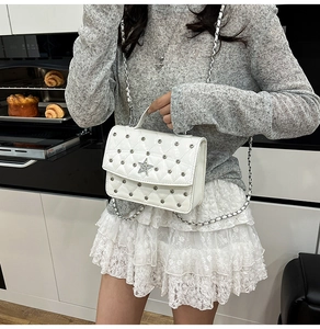 Detail of white quilted crossbody bag with star ornament and metal rivets in a lifestyle setting