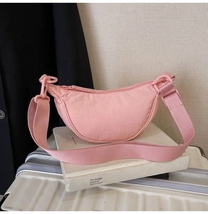 Detail of a pink nylon crescent shoulder bag placed on white books for lifestyle display