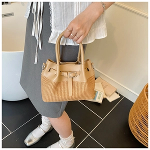 Detail view of woven straw bucket bag with leather handles and metallic buckles