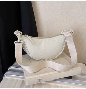 Minimalist creamy white nylon half-moon shoulder bag styled on travel suitcase