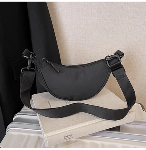 Detail view of a black nylon crescent bag with wide strap on a white suitcase