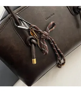 Dettaglio della borsa tote marrone scuro con logo metallico e ciondolo a racchetta