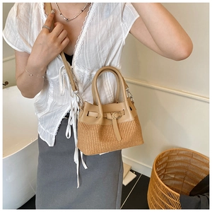Detail of woven straw and khaki leather bucket bag held by hand in a minimalist setting