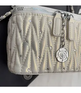 Detail of white quilted handbag with crystal embellishments and camellia flower pendant