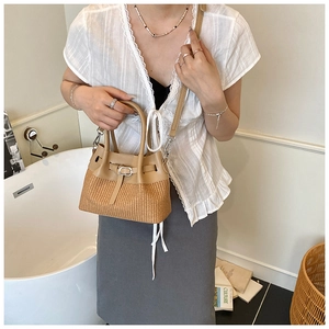 Detailed view of bicolor woven straw handbag with premium leather handles and metal hardware