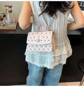 Detail of pink quilted crossbody bag with rhinestone star logo on a white lace shirt