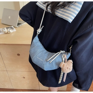 Detail der hellblauen Denim-Halbmondtasche mit Metallknoten und einem Plüschbär-Anhänger