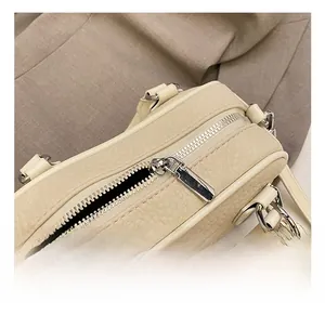 Detailed close-up of premium lychee texture leather and silver metal zipper on beige bag