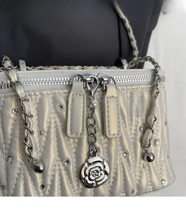 Close-up of silver quilted bag featuring a camellia flower charm and dual zipper detail
