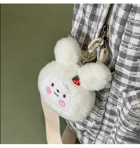 Detail of white plush bunny keychain with strawberry embroidery on a checkered backpack
