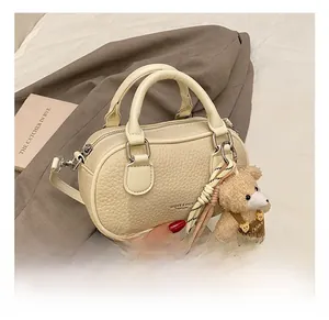 Close-up of cream lychee texture bowling bag with bear charm and adjustable strap