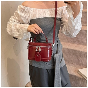 Détail du sac boîte verni bordeaux avec fermetures éclair argentées et bandoulière réglable