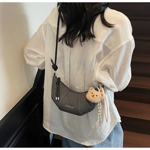 Detail der grauen sichelförmigen Tasche mit Druck und süßem Plüschbär-Anhänger und Aufdruck