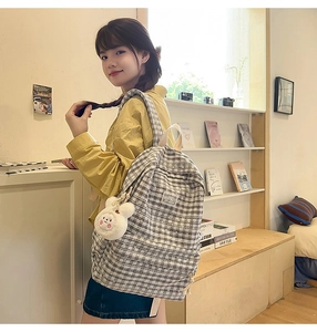 Detail of grey plaid backpack featuring a white plush bunny charm and stitched label