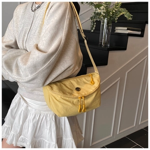 Detail of a bright yellow casual nylon crossbody bag with a round metal logo and dual zippers