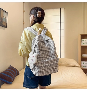 Grey plaid canvas backpack on model featuring front pocket and white plush bunny charm
