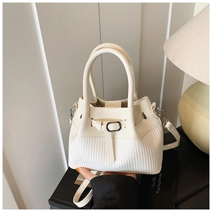 Detail of cream white bucket bag featuring woven texture and smooth leather panel with strap
