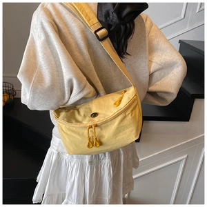 Detail of yellow nylon crossbody bag featuring dual zippers and adjustable fabric strap