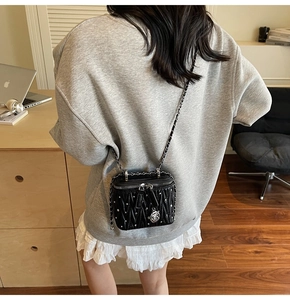 Detail of black quilted leather crossbody bag with silver studs and rose pendant accessory