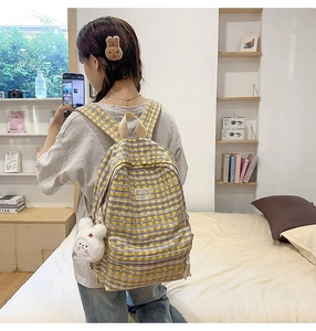 Close-up of a plaid canvas backpack featuring a yellow and purple grid and plush bunny charm