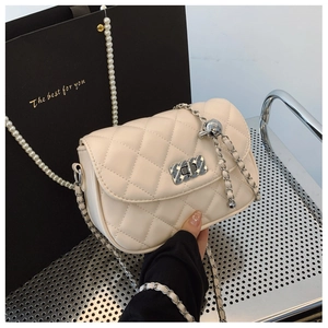 Macro detail of cream quilted crossbody bag with silver chain and metal tassel