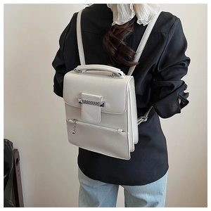 Detail einer cremeweißen Lederhandtasche mit Kettenverzierung und Akkordeon-Struktur