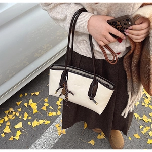 Dettaglio della borsa tote crema con spalline marroni e ciondolo a cavallo in autunno