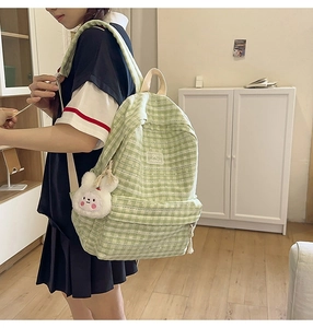 Detail of light green plaid backpack with white bunny plush charm and STANGE label