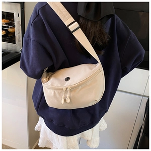 Detail of a beige crescent nylon crossbody bag with adjustable strap and dual zippers