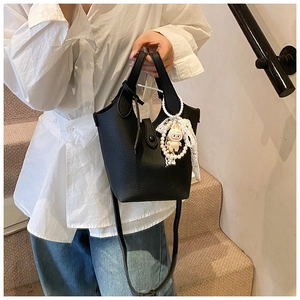 Detail of black leather bucket bag with litchi texture and rabbit pearl charm