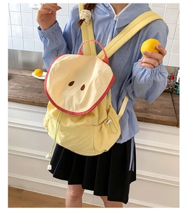 Detail of yellow round backpack with red piping and green drawstrings shown on model