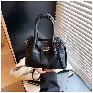 Detail of black bucket bag featuring smooth leather and woven texture with silver buckle