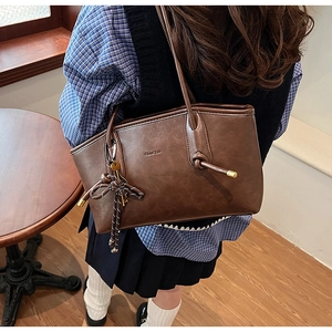 Dettaglio di borsa tote vintage marrone scuro con ciondolo in metallo e trama