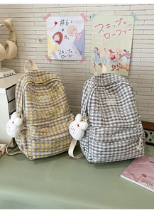 Detail of plaid canvas backpacks with plush bunny charms and stylish checkered patterns