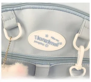 Détail du sac à dos en toile bleu clair avec logo en cuir blanc et pompon en peluche doux