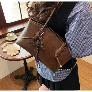 Dettaglio borsa tote in pelle marrone scuro con corda intrecciata e ciondoli decorativi